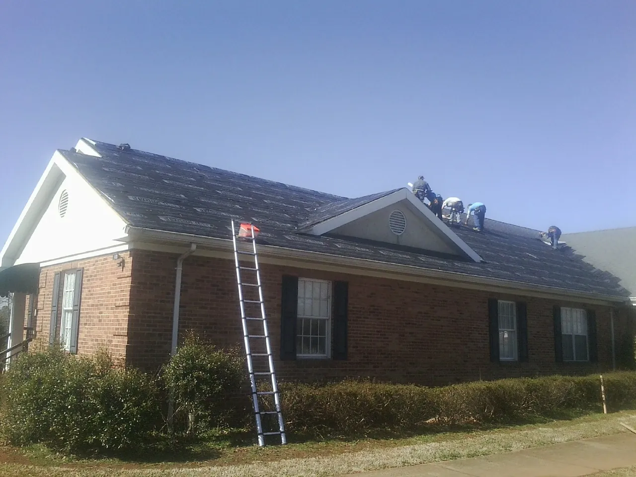 Crew tearing shingles off a brick ranch roof with a ladder set — Metal Roof Repair work by our crew in Osseo