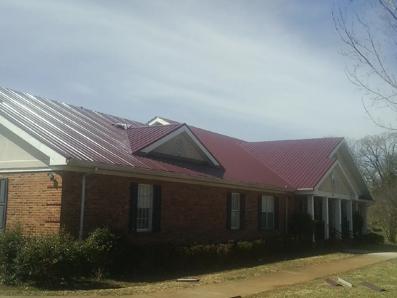 Red metal roof with gabled entries on a long brick building, from a Hail Damage Roof Repair job in Osseo