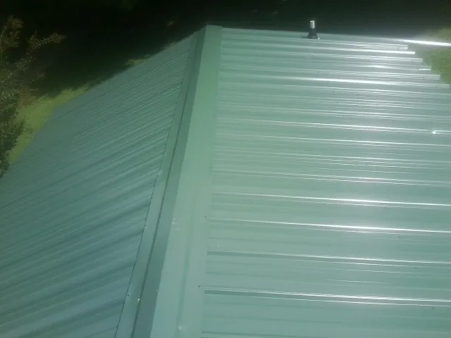 New green metal panels meeting at the ridge of a roof — Flat Roof Repair work by our crew in Osseo