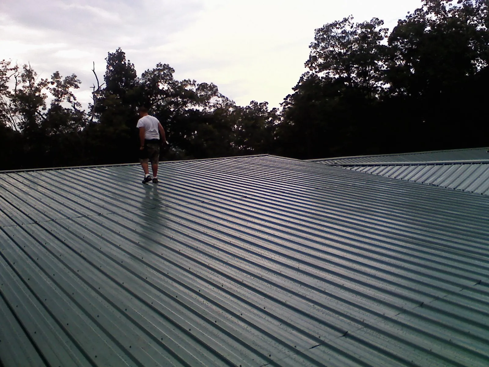 Roofer walking a wide expanse of new green metal roofing in Osseo