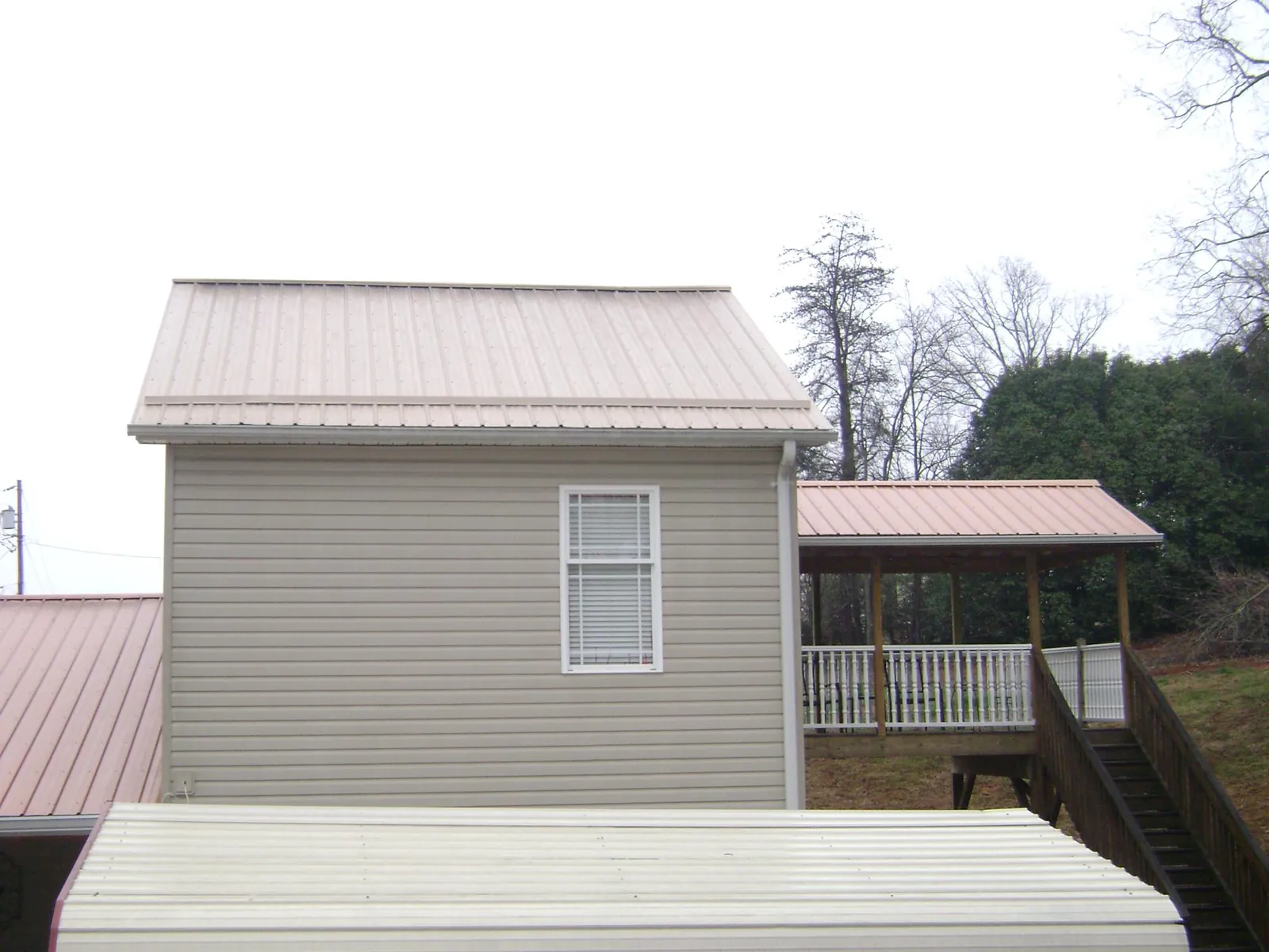 Tan metal roofs on a two story addition and attached porch, from a Roof Replacement job in Osseo